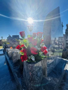 Vase de roses rouges déposé sur une tombe sous un soleil éclatant.
