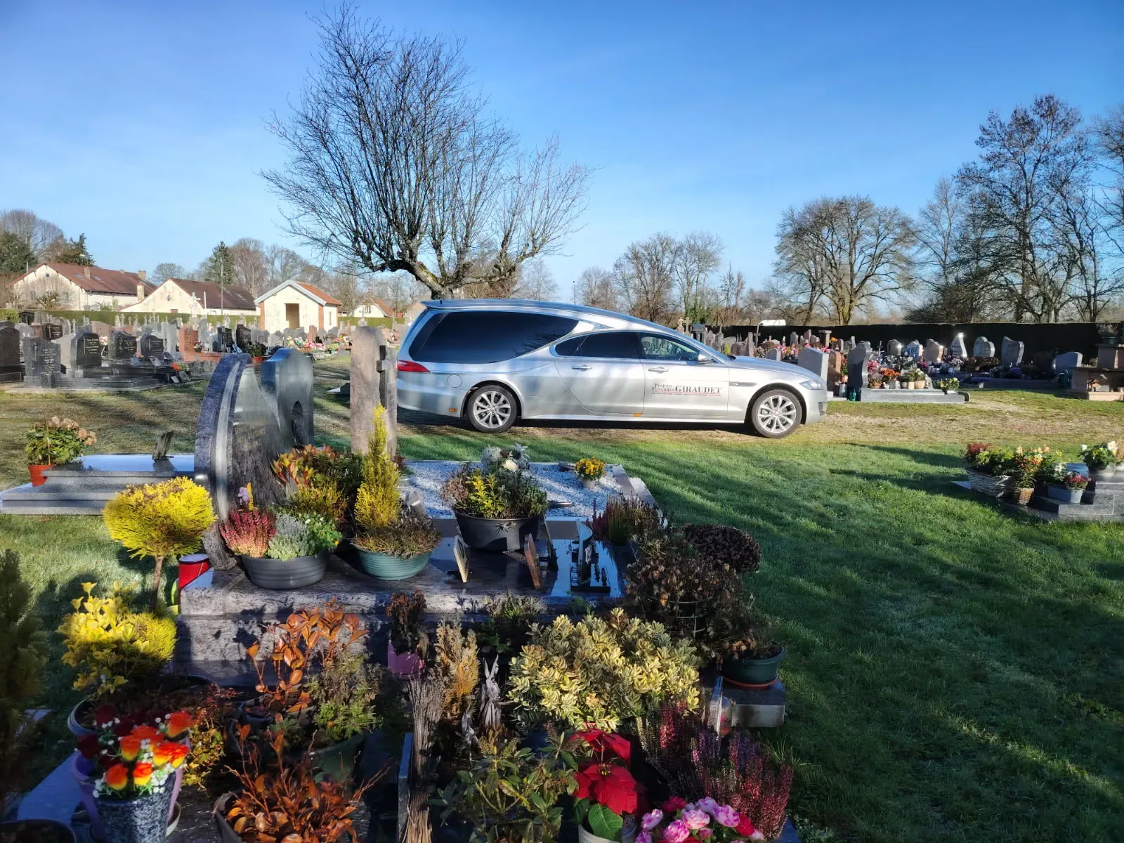 Corbillard gris garé dans un cimetière paysager près des tombes.